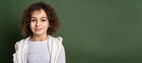 One small caucasian girl ten years old with curly hair front view portrait close up standing in front of green background looking to the camera smiling happy and joy copy space
