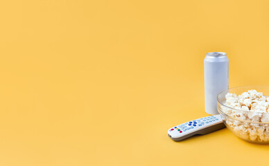 Remote control, popcorn and can of beer on yellow background. The concept of family watching movies and TV shows. Selective focus, copy space.
