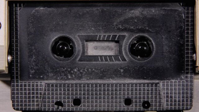 Stopping and removing an old black unlabeled cassette tape from a deck, and putting it back. Retro vintage worn magnetic media, nostalgic vibes. Front shot.
