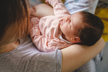 Unknown caucasian woman holding her newborn baby two weeks old at home - infant girl in arms of her mother feeling safe sleeping or taking a nap - childhood growing up and parenthood concept