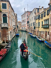 Fototapeta na wymiar A gondolier travels along a beautiful, azure green canal in Venice surounded by the famous pink, stone buildings. Taken in winter. Venice - Italy