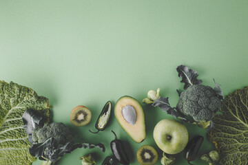 Creative layout food concept made of green fruit and vegetables on green background flat lay: avocado, kale, broccoli, Brussels sprouts, kiwi, peppers, apple, cabbage top view with space for text
