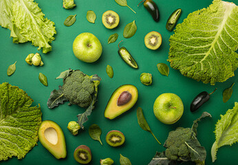 Creative layout healthy organic food concept made of green fruit and vegetables on green background flat lay: avocado, kale, broccoli, Brussels sprouts, kiwi, peppers, apple, cabbage top view
