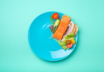 Intermittent fasting low carb hight fats diet concept flat lay, healthy food salmon fish, bacon meat, vegetables and salad on blue plate and blue background top view 