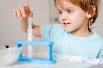 Happy boy in blue T-shirt conducts chemical experiments with vinegar and soda at home