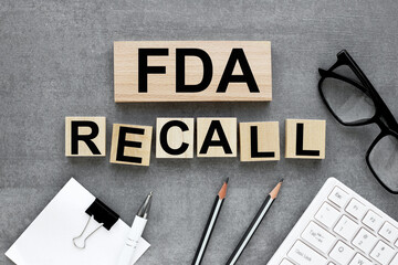 FDA recall text on wood blocks near keyboard and glasses on gray background. business concept