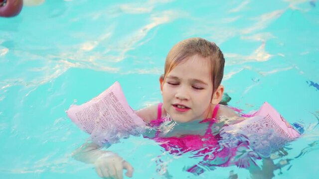 a funny little girl swims in inflatable armbands in a pool near the buoys. 
