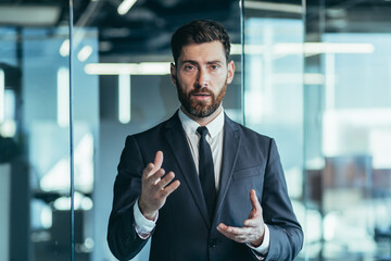 Serious and focused businessman listening to a talk report, video link, portrait of a successful man in a business suit looking at the camera