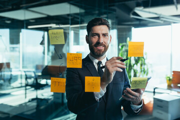 Portrait of a successful businessman near a glass board with tasks, the man fulfilled his plan on time, rejoices and celebrates victory