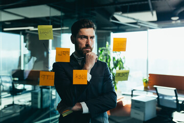 businessman in reflection at a glass task board, hangs plans on colored paper stickers, plans for the near future