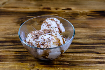 Glass bowl with ice cream balls and chocolate topping on a wooden table