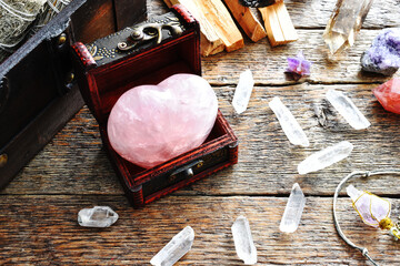 A top view image of a heart shaped rose quartz crystal in a small wooden box. 