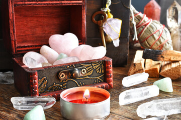 A low angle image of rose quartz crystals in a small wooden box with a lit red candle. 