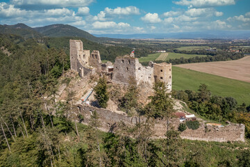 Aerial view of under restoration medieval Reviste castle above the Hron (Garam) river in Slovakia with donjon, circular gate tower, ruined gothic palace blue cloudy sky 