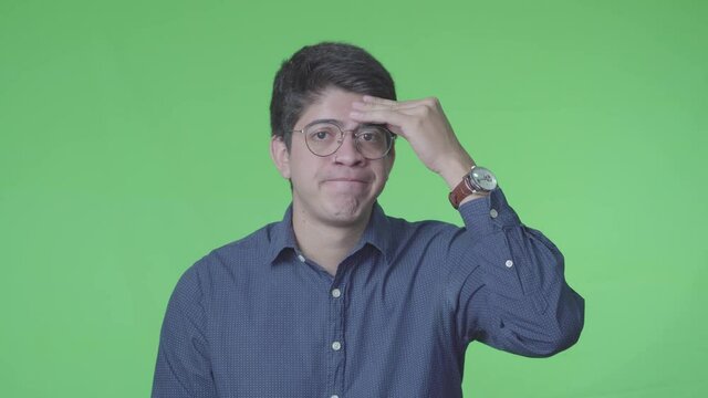 Hombre latino decepcionado negando con su expreci&oacute;n y fondo verde