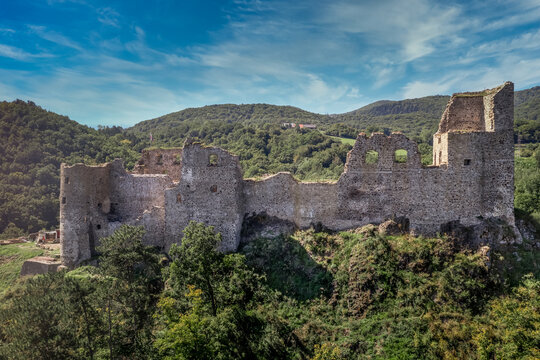 Aerial view of under restoration medieval Reviste castle above the Hron (Garam) river in Slovakia with donjon, circular gate tower, ruined gothic palace blue cloudy sky 