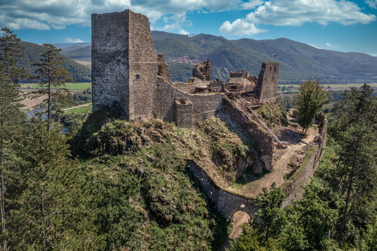 Aerial view of under restoration medieval Reviste castle above the Hron (Garam) river in Slovakia with donjon, circular gate tower, ruined gothic palace blue cloudy sky 