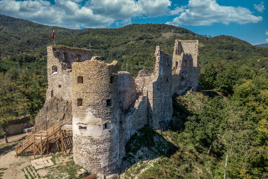 Aerial view of under restoration medieval Reviste castle above the Hron (Garam) river in Slovakia with donjon, circular gate tower, ruined gothic palace blue cloudy sky 