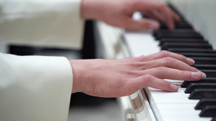 Close-up hands of a young man in a white jacket play music on the piano.Classical music, concert, performance.Music lessons on the piano, keyboard instrument.Macro photography.Selective focus.