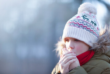 The boy is warming his hands outside in winter