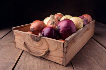Onions in old box on rustic wooden table, food ingredients