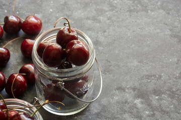 Ripe and juicy cherries on table in jars, dark background, selective focus 