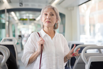 European senior woman with handbag standing in tram and waiting for her stop.