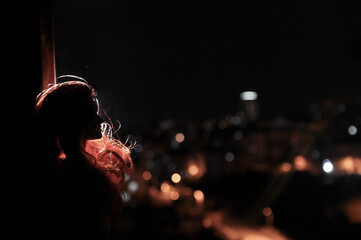 Silhouet van een vrouwelijk gezicht op een lichte achtergrond. SIlhouette van een eenzame pop met lang haar & 39 s nachts met achtergrondverlichting van uitzicht op de stad vanuit raam