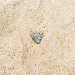 Heart-shaped gray sea rock on sandy beach, square photo