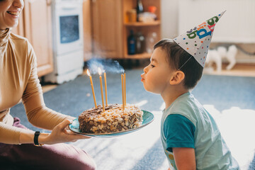 Side view of an caucasian little boy blowing out candles on birthday cake at his party. Candles...