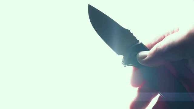 Sharp knife in male hand. EDC automatic folding pocket knife opening blade on white background with lens flare, toned