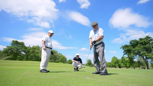 Group of Asian people businessman and senior CEO golfing near the hole on golf fairway together at country club. Healthy elderly man golfer enjoy outdoor golf sport and leisure activity with friends.