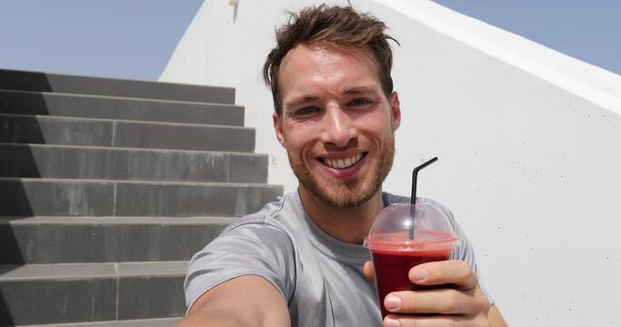 Selfie video by healthy eating man drinking beet juice smoothie in urban city background. Active lifestyle fitness runner eating breakfast vegetable shake on stairs after run