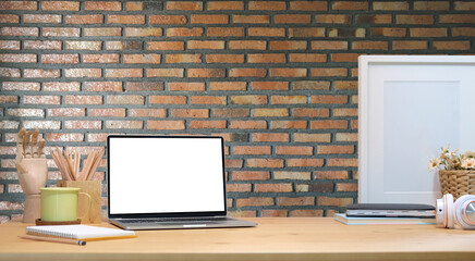 Mock up computer laptop, supplies and empty frame on wooden table with brick wall.