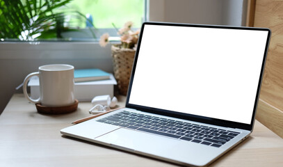 Computer laptop with blank screen and coffee cup on wooden table near window.