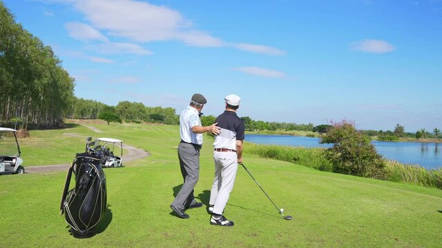 4K Asian people senior man teaching his adult son hitting golf ball on golf course. Healthy elderly male golfer enjoy leisure activity outdoor sport golfing at golf country club in summer vacation