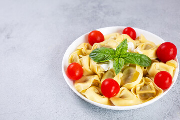 Ravioli with tomato and basil on gray background