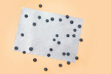 heaps of blueberries are scattered on a shiny gray leaf on a beige background