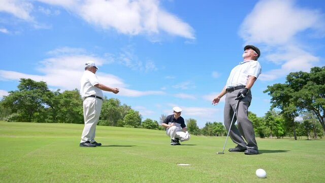 Group of Asian people businessman and senior CEO golfing near the hole on golf fairway together at country club. Healthy elderly man golfer enjoy outdoor golf sport and leisure activity with friends.
