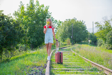 naughty woman with a hat walks on the rails with a suitcase