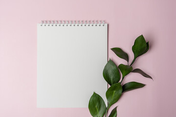 white spiral notebook for notes with copy space on a pink background with a plant leaf top view spring mood