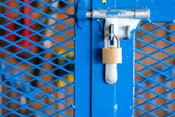 A key padlock is locking on metal fence gate knob of the hand tool storage box (as blurred backgroung). Industrial object photo. Close-up and selective focus. - Powered by Adobe