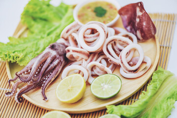 squid rings on wooden plate, Fresh squid cooked boiled with lettuce vegetable salad lemon and seafood sauce on table background