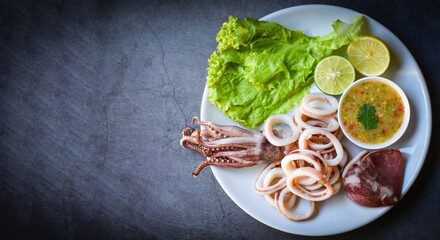 squid rings on white plate, Fresh squid cooked boiled with lettuce vegetable salad lemon and seafood sauce on black background, top view