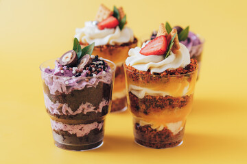 Puff muffins with berries and cookies in glasses on yellow background.