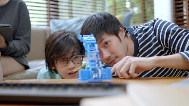 Remote learn online at home concept.asian boy child student remotely learn with father and mother in coding control robot arm on laptop and electronic board cable in STEM,robotics engineer at home.