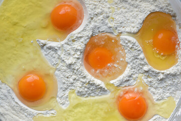 Five broken eggs lie in a plastic bowl made of flour and are photographed from above. You can see...