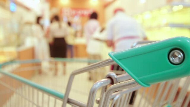 New normal concept close up handle of shopping cart in supermarket with blur people wear protective face mask walk for shopping after covid-19, coronavirus outbreak