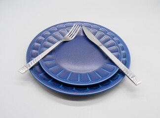 白い背景に置かれた紺色のお皿（2枚）とカトラリー（ナイフ及びフォーク）