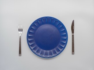 白い背景に置かれた紺色のお皿とカトラリー（ナイフ及びフォーク）